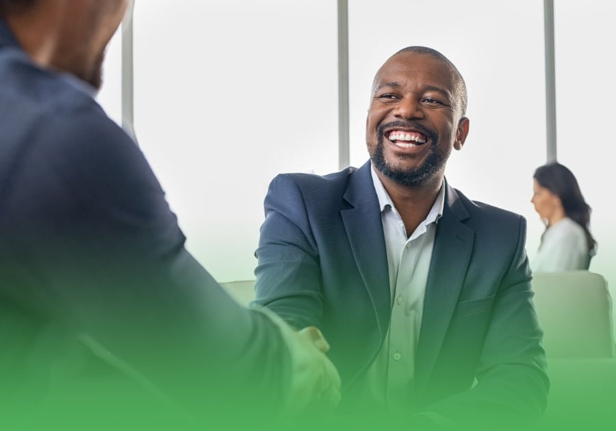 two African American professionals in suits sitting down and shaking hands