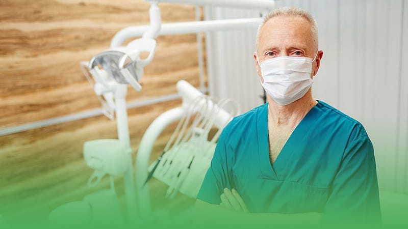 Dental clinic business owner wearing surgical mask stands before dental chair.