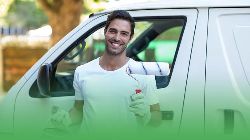 Happy painting business owner poses with paint roller in front of van.