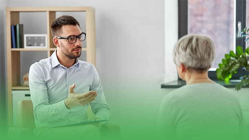 Psychiatrist business owner converses with elderly woman seated in chair.