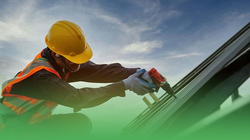 Construction worker from roofing business using drill to create hole on roof.