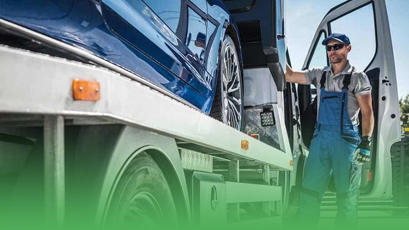 Towing business owner stands beside truck accompanied by blue car.