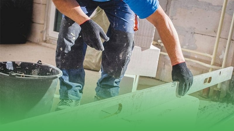 Man in blue shirt and black gloves diligently works on wall skillfully practicing masonry techniques.