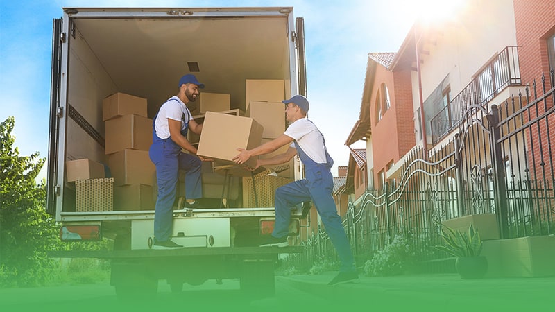 Two workers in blue overalls efficiently load boxes into moving truck showcasing professionalism of moving company.