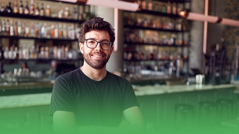 Restaurant business owner wearing glasses standing in front of bar.