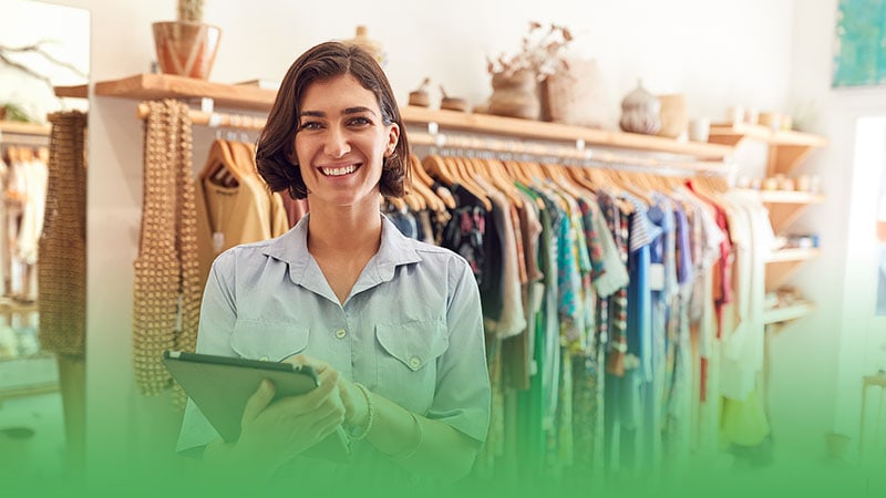 Retail business owner stands before rack of clothes selecting items for store.